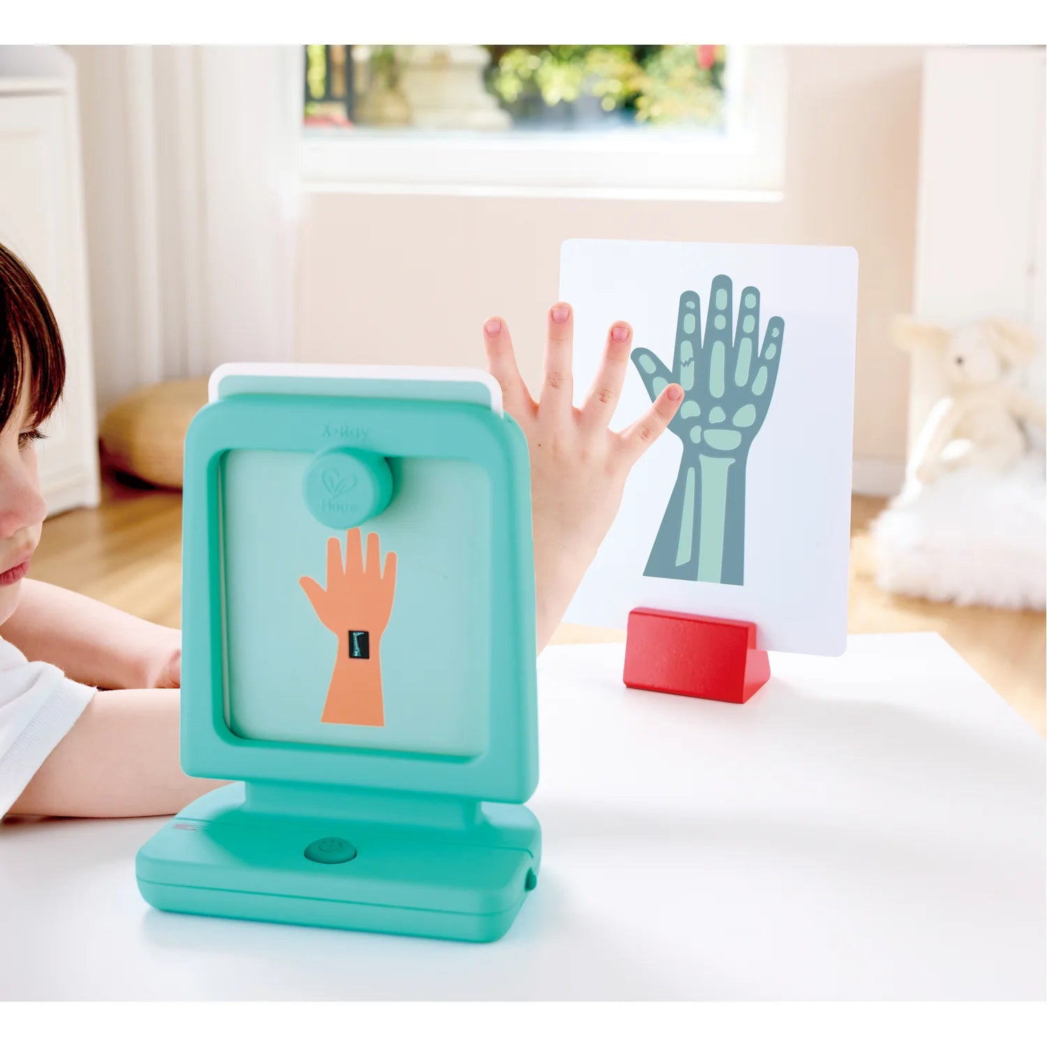 Teal educational tool with hand illustrations on a table, child's hand reaching out.