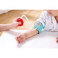 Baby's arm with a blood pressure monitor and a hand holding a red device on a light-colored surface.