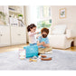 Two children playing with a toy kitchen set in a living room.