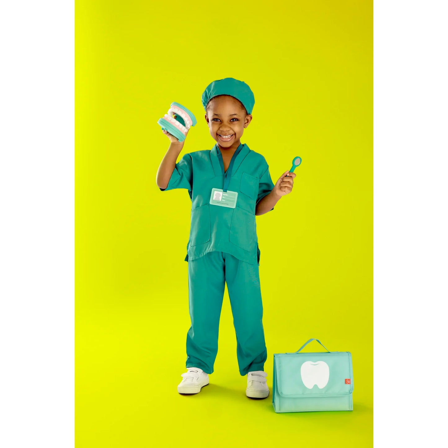 Child in green medical scrubs with a toy stethoscope and bag on a yellow background