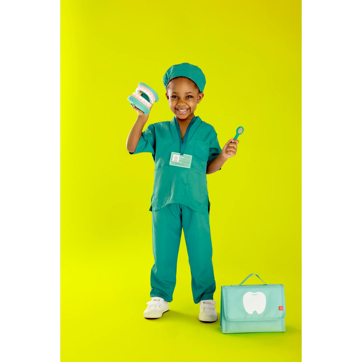 Child in green medical scrubs with a toy stethoscope and bag on a yellow background