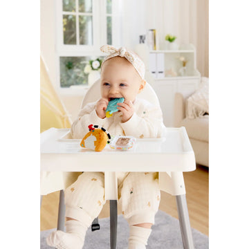 Baby in a high chair with toys, sitting in a bright room.