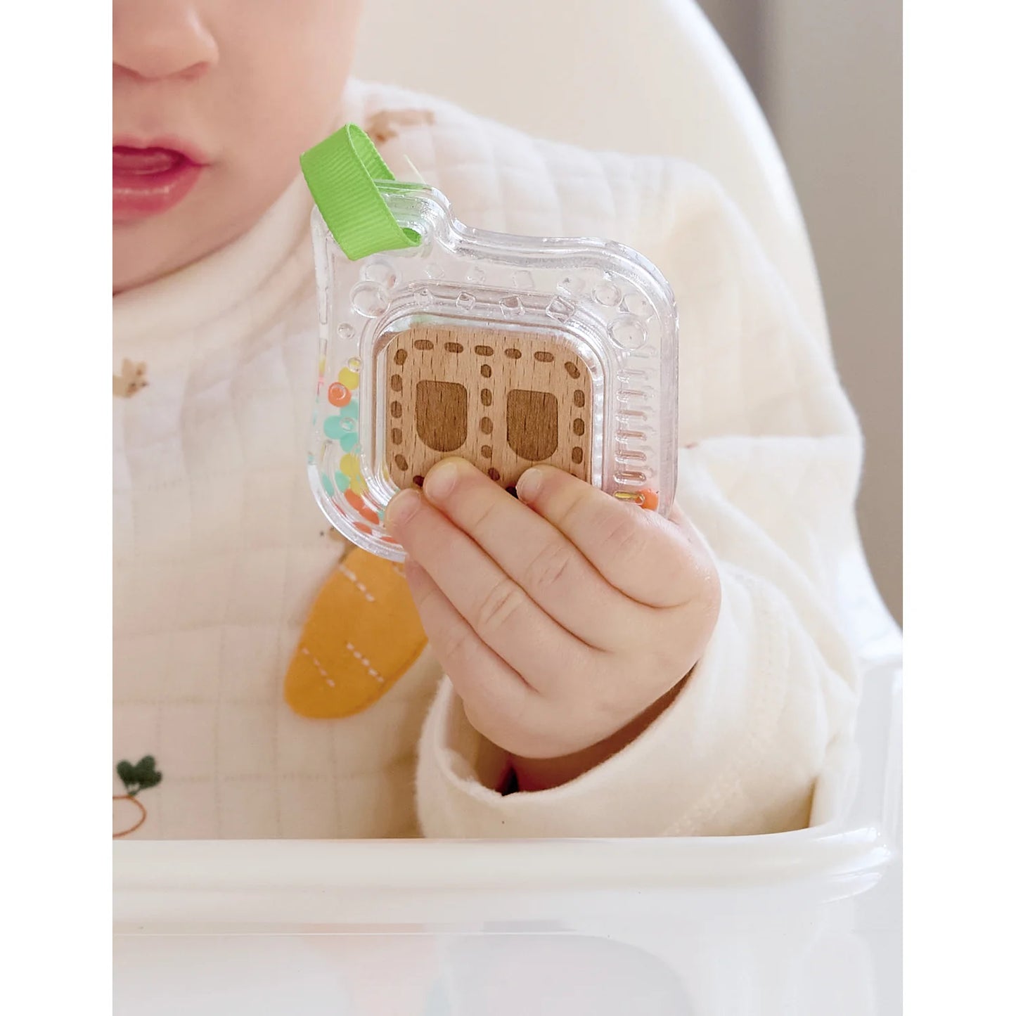 Baby holding a small wooden toy in a clear plastic package with a green label.