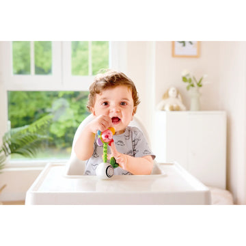 Baby sitting in a high chair with a colorful toy, surrounded by a bright room with a window and plants.