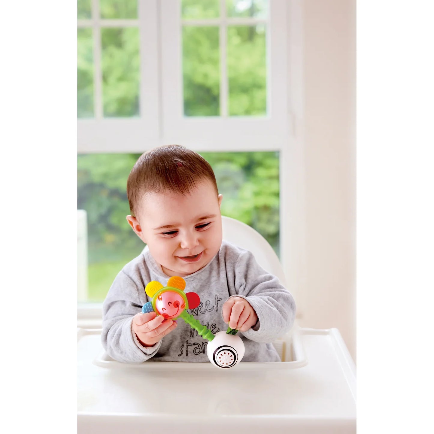 Baby playing with a colorful toy in a bright room with a window in the background
