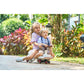 Two children riding a scooter in a garden setting with greenery and flowers.