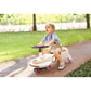 Child riding a toy car on a path with grass and trees in the background
