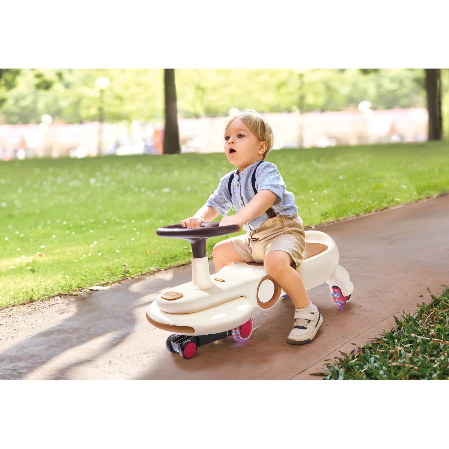 Child riding a toy car on a path with grass and trees in the background