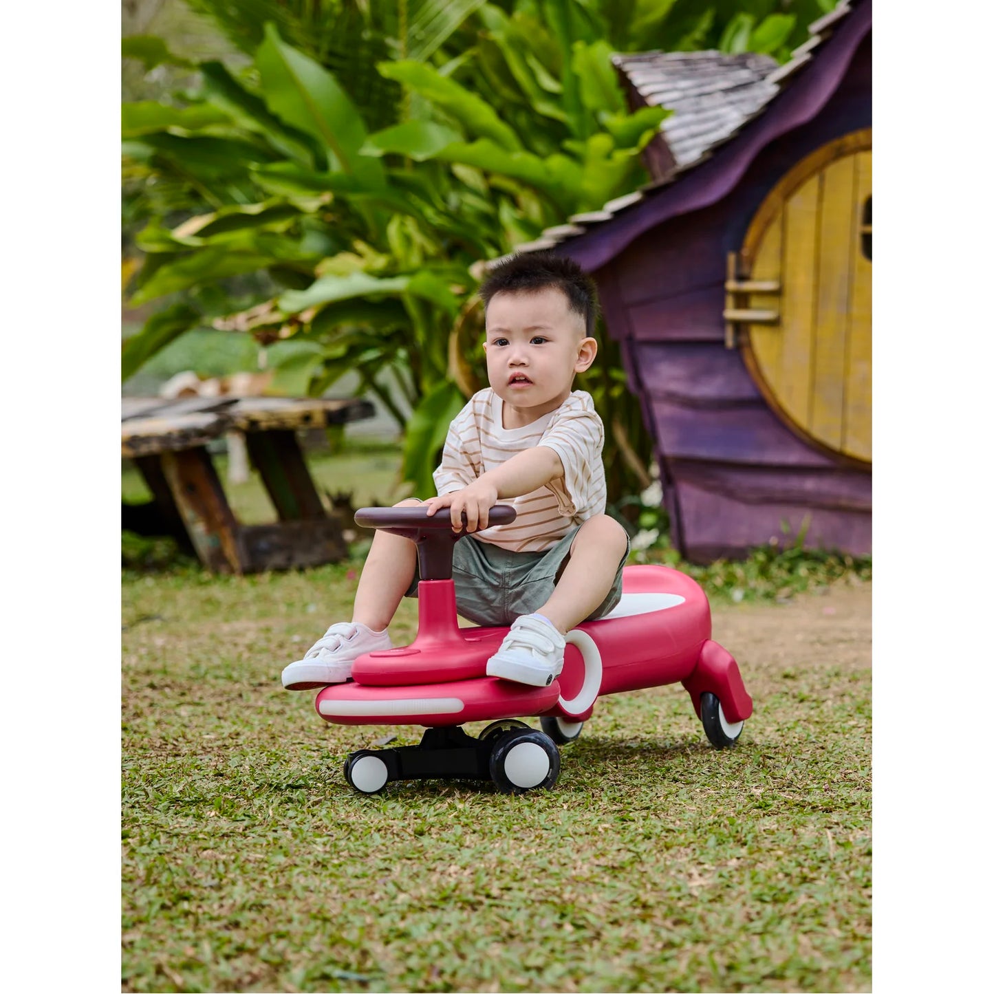 Child sitting on a pink toy car in a garden setting