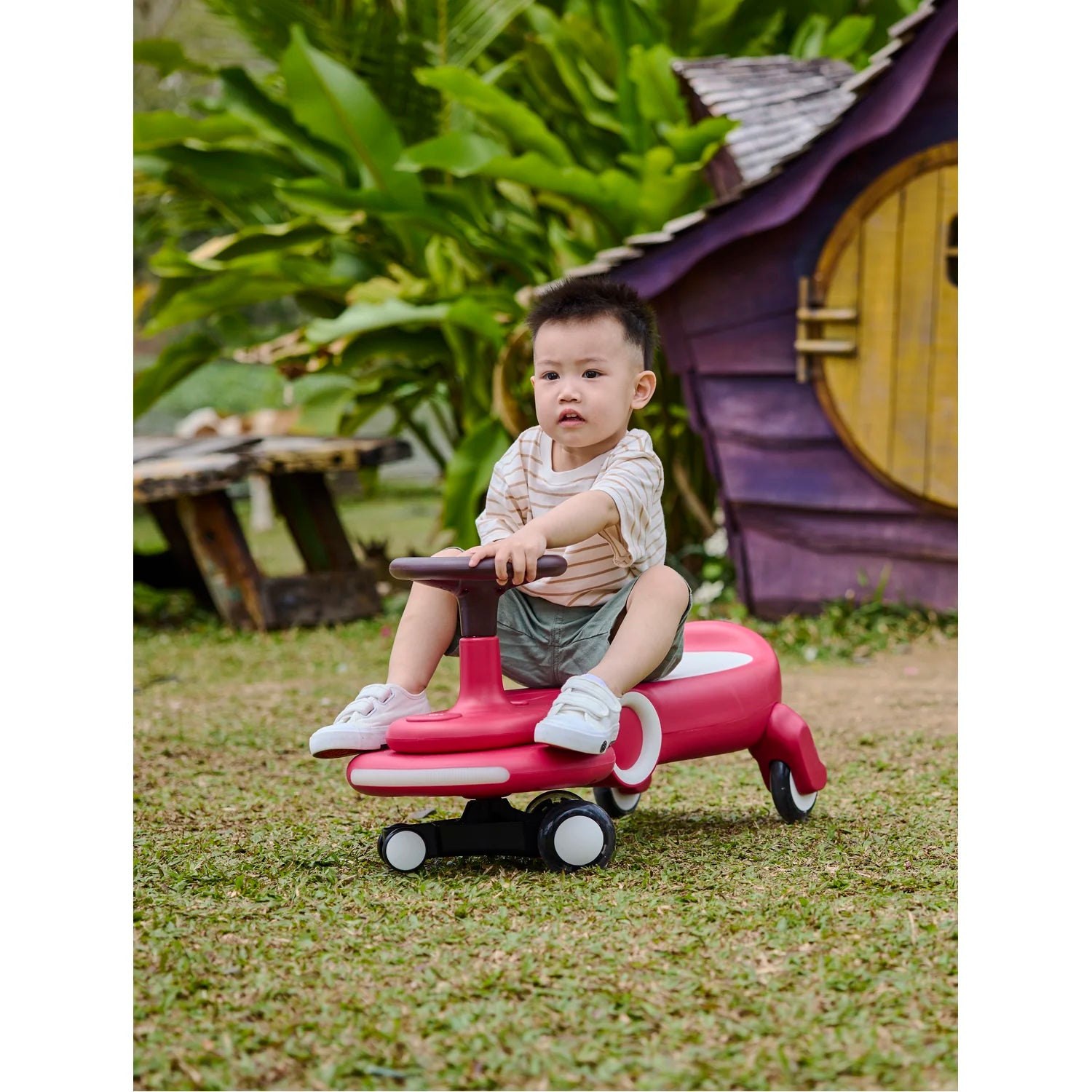 Child sitting on a pink toy car in a garden setting