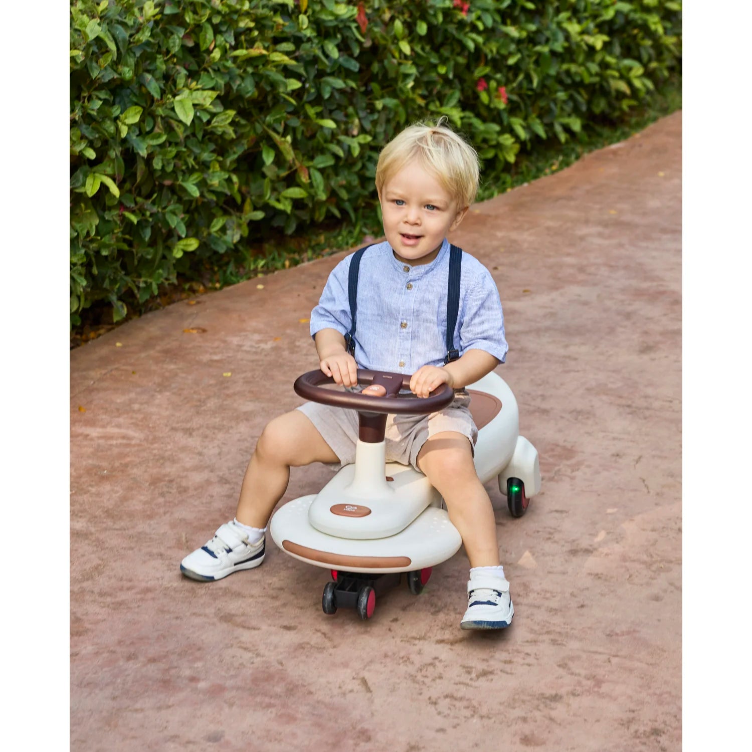 Child sitting on a toy car with a steering wheel outdoors.